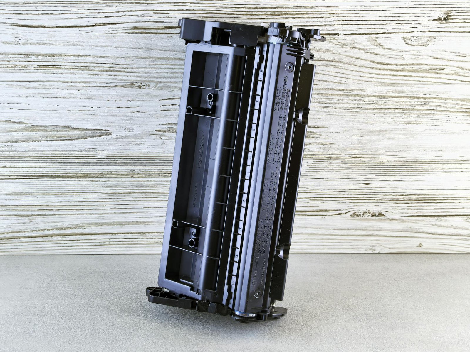 Close-up of a black printer toner cartridge against a rustic wooden background, side view.